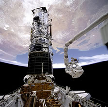 Astronaut F. Story Musgrave, anchored on the Space Shuttle Endeavor's robotic arm, prepares to be elevated to the top of the Hubble Space Telescope during Hubble's first servicing mission in 1993. Click on image to go to Hubble Site